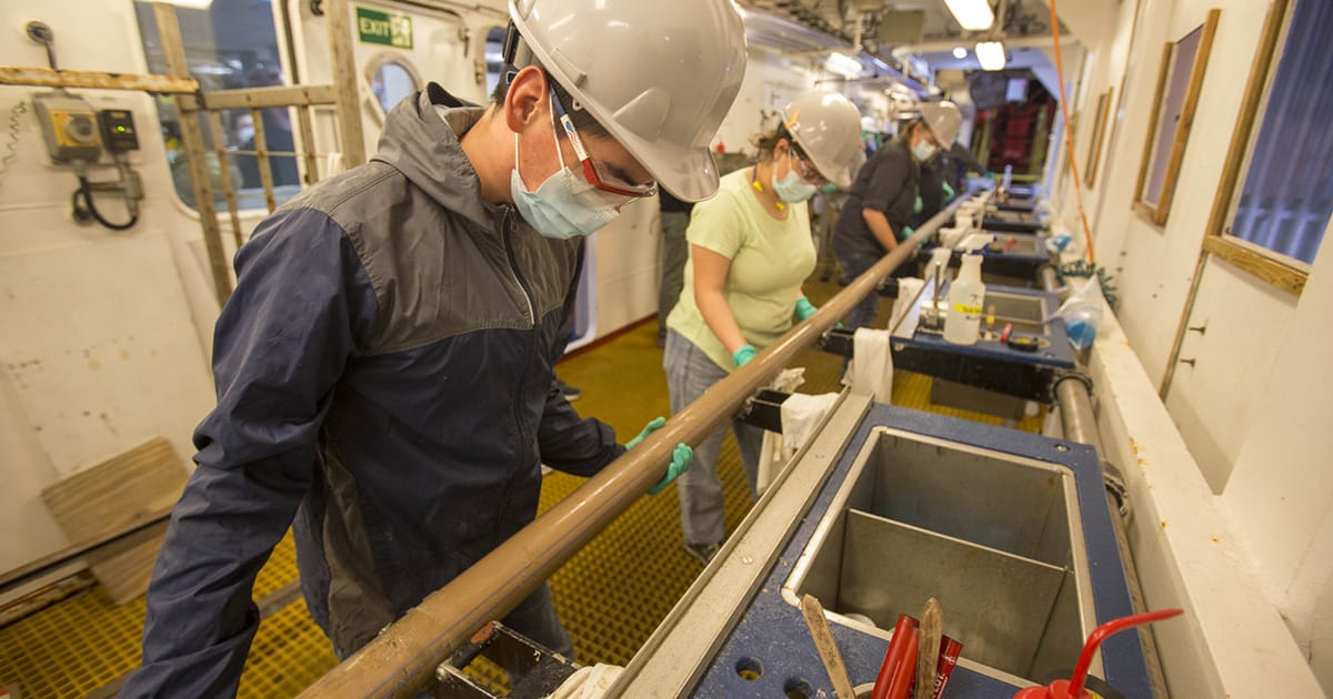 Above left, Oscar Cavazos (Marine Laboratory Specialist, IODP JRSO) joins other marine techs in preparing a new sediment core to be sectioned on the catwalk of JOIDES Resolution in 2022.