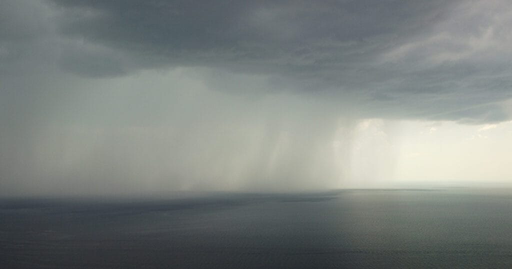 Aerial view footage of rain clouds over sea ocean Black clouds in bad weather day over sea surface High angle view nature view Apocalypse. Storm Large freight dark gloomy rain clouds over a calm sea.