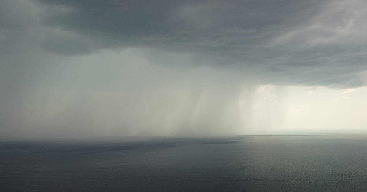 Aerial view footage of rain clouds over sea ocean Black clouds in bad weather day over sea surface High angle view nature view Apocalypse. Storm Large freight dark gloomy rain clouds over a calm sea.