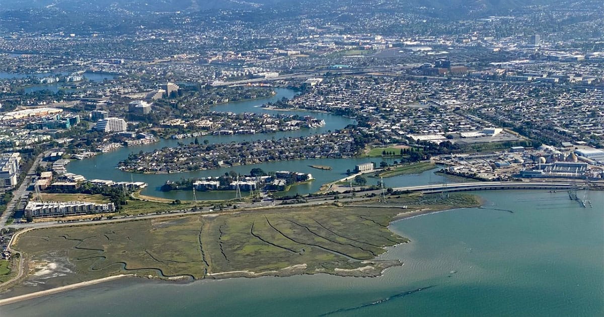 An aerial view of marshes on Bair Island in San Francisco Bay in front of the low-lying homes and businesses of the Redwood Shores community.