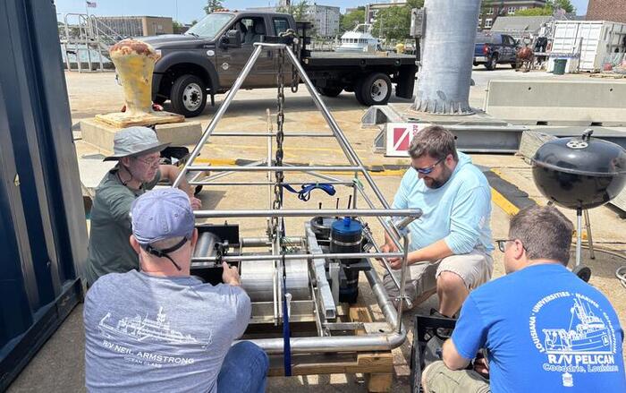 four people around a large piece of equipment outside by the water