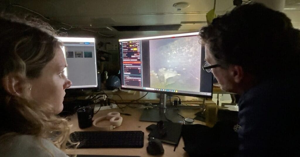 WHOI imaging specialists Dwight Coleman (right, also the Chief Scientist of the Heroic Age Expedition) and Zoe Daheron (left) watch as real-time images of the wreck of Sir Ernest Shackleton’s Quest are transmitted from the seafloor off the coast of Labrador and Newfoundland to a lab on the research vessel Atlantis. (Photo by Ken Kostel, © Woods Hole Oceanographic Institution)
