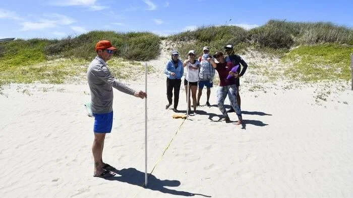 A sandy beach scientist gives pointers to visiting researchers on how to use two PVC poles to measure the slope. (Image credit: TAMUG Division of Marketing and Communications)